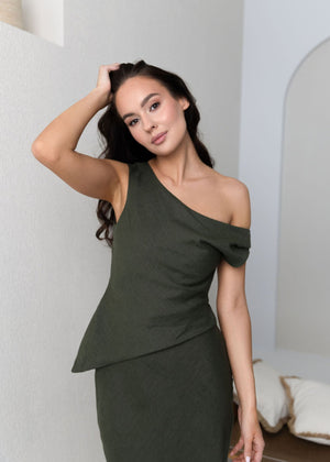 Woman wearing a green linen one-shoulder dress posing indoors.