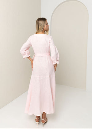 Woman wearing a light pink linen dress standing in a minimalistic room with a white wall and arch.