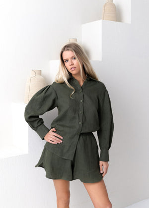 Woman wearing a green outfit standing in a minimalistic setting.