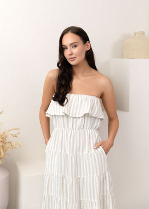 Woman wearing a white linen strapless dress with ruffled layers against a white background