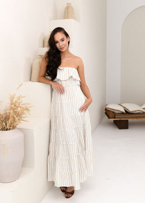 Woman in a white strapless dress standing in a minimalistic room with white walls and a wooden bench.
