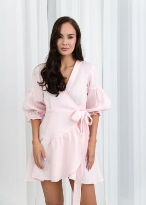 Woman wearing a light pink linen dress against a white curtain background