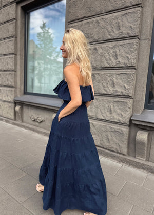 Woman in a Bohomey navy blue maxi linen dress standing against a stone building.