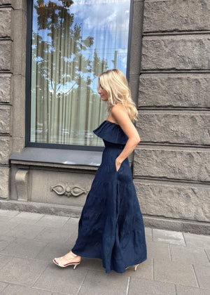 Woman in a Bohomey navy blue linen dress standing on a sidewalk with a stone building in the background