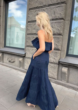 Woman wearing a Bohomey blue long linen dress standing in front of a building with large windows.