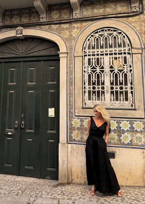Woman in a Bohomey black linen maxi dress standing in front of a decorative building with tiled facade.