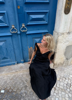 Woman in a Bohomey black linen dress sitting in front of a blue door.