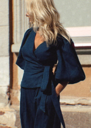 Woman in a navy blue linen suit walking on a street with a building in the background