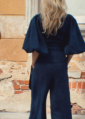 Woman wearing a navy blue linen suit standing against a textured wall.