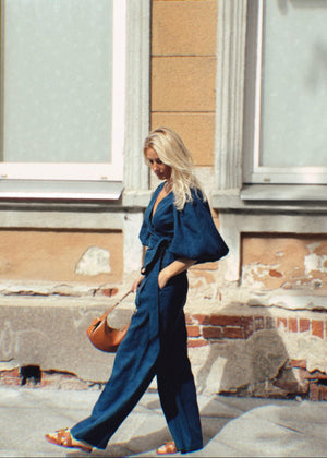 Woman in a blue linen suit walking on a street with a building in the background