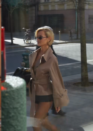 Woman walking on a city street wearing a beige coat and sunglasses.