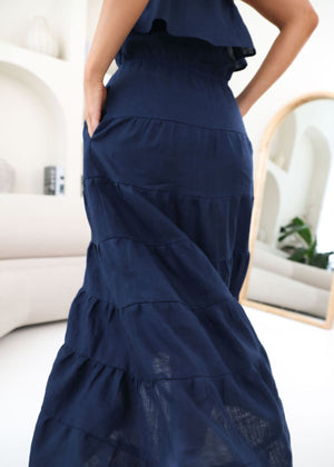 Navy blue dress with ruffled layers worn by a person, sitting on a white couch.