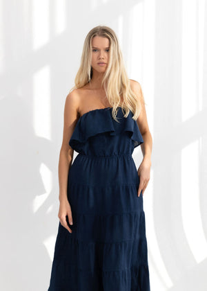 Woman wearing a linen navy blue strapless dress with ruffled layers on a white background
