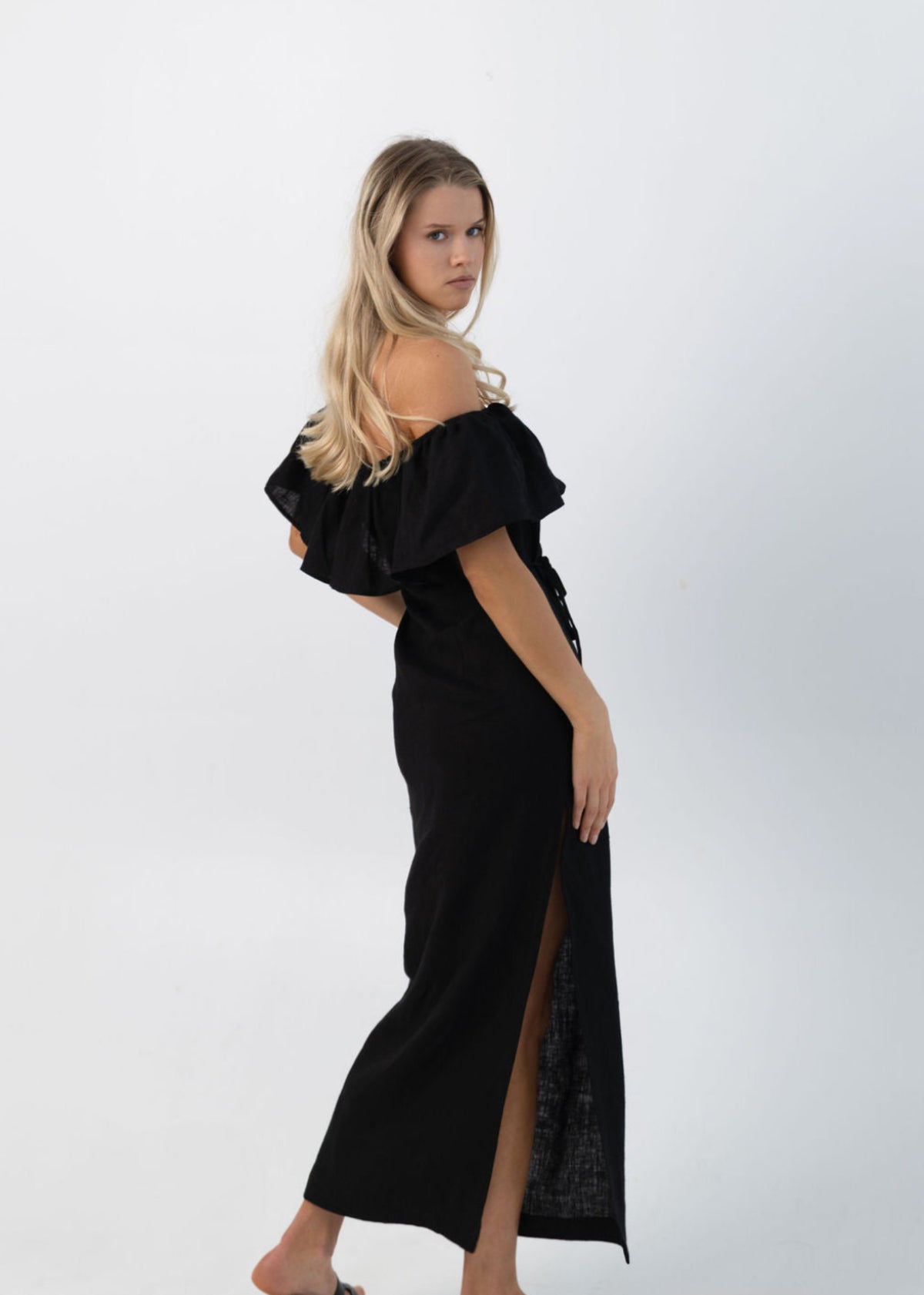 Woman wearing a black linen off-shoulder dress with a slit on a white background