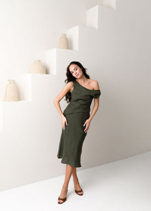 Woman in a green linen dress standing against a white wall with geometric shapes.