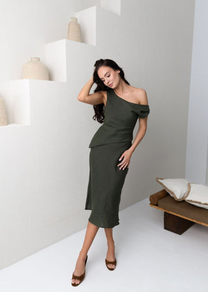 Woman in a green linen off-shoulder dress posing in a minimalistic setting.