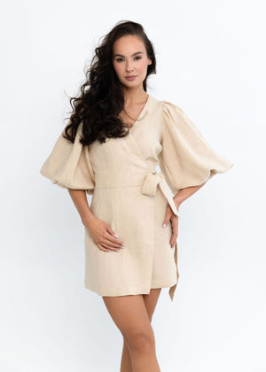 Woman wearing a beige linen dress with cape sleeves on a white background