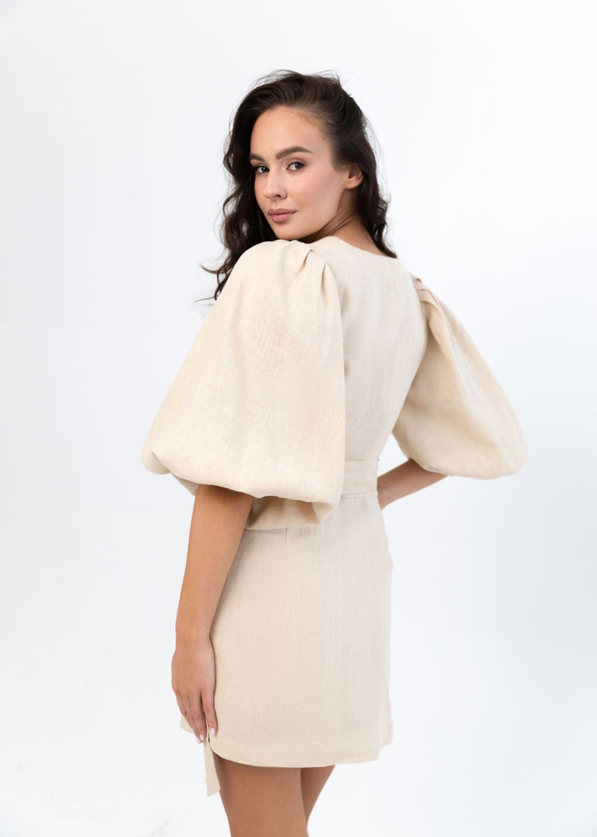 Woman wearing a beige linen dress with puffed sleeves on a white background