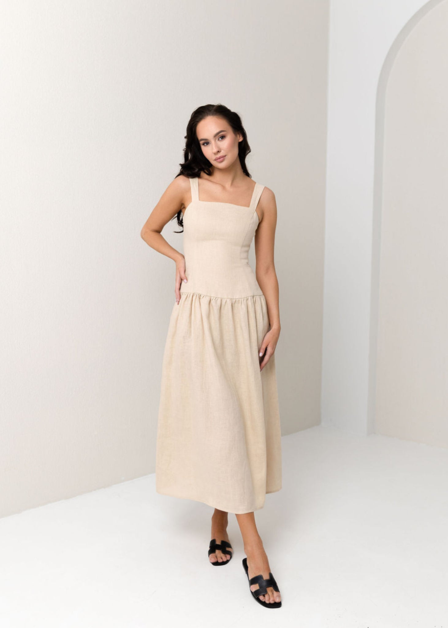 Woman wearing a beige linen dress in a minimal white room