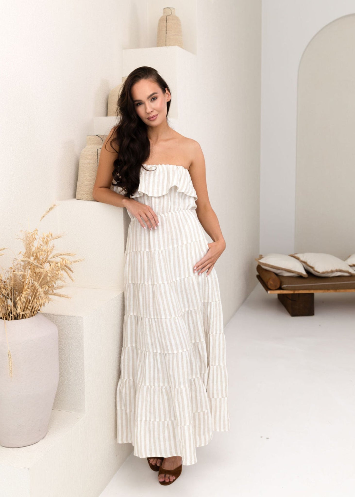 Woman wearing a white linen strapless dress with ruffled details against a neutral background