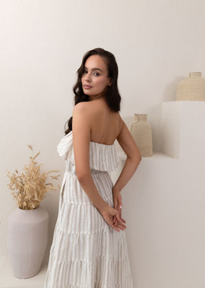 Woman in a white linen dress standing in a minimalistic room with a vase and plant.