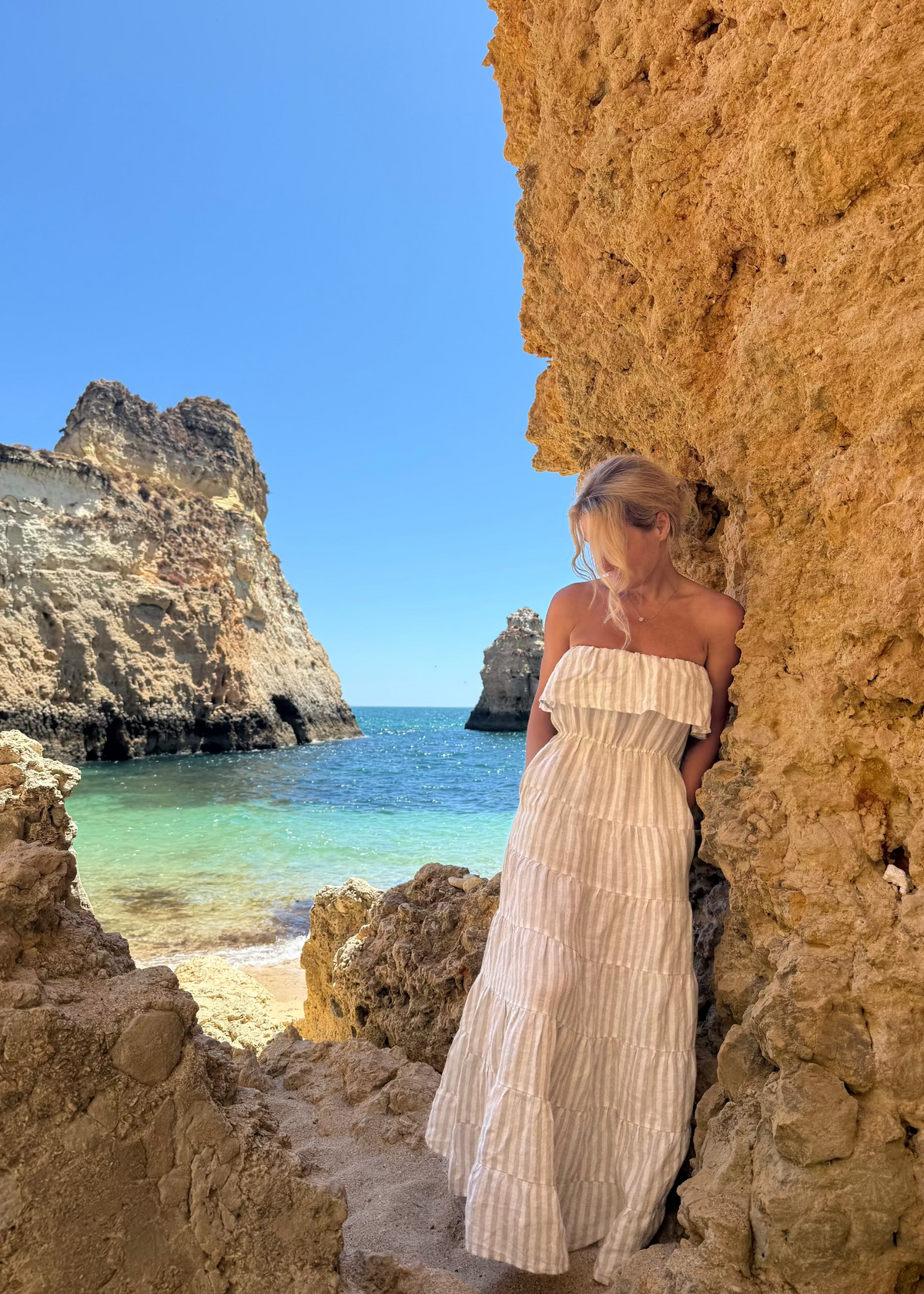 Woman in a Bohomey light linen dress standing in a natural rock formation by the ocean.