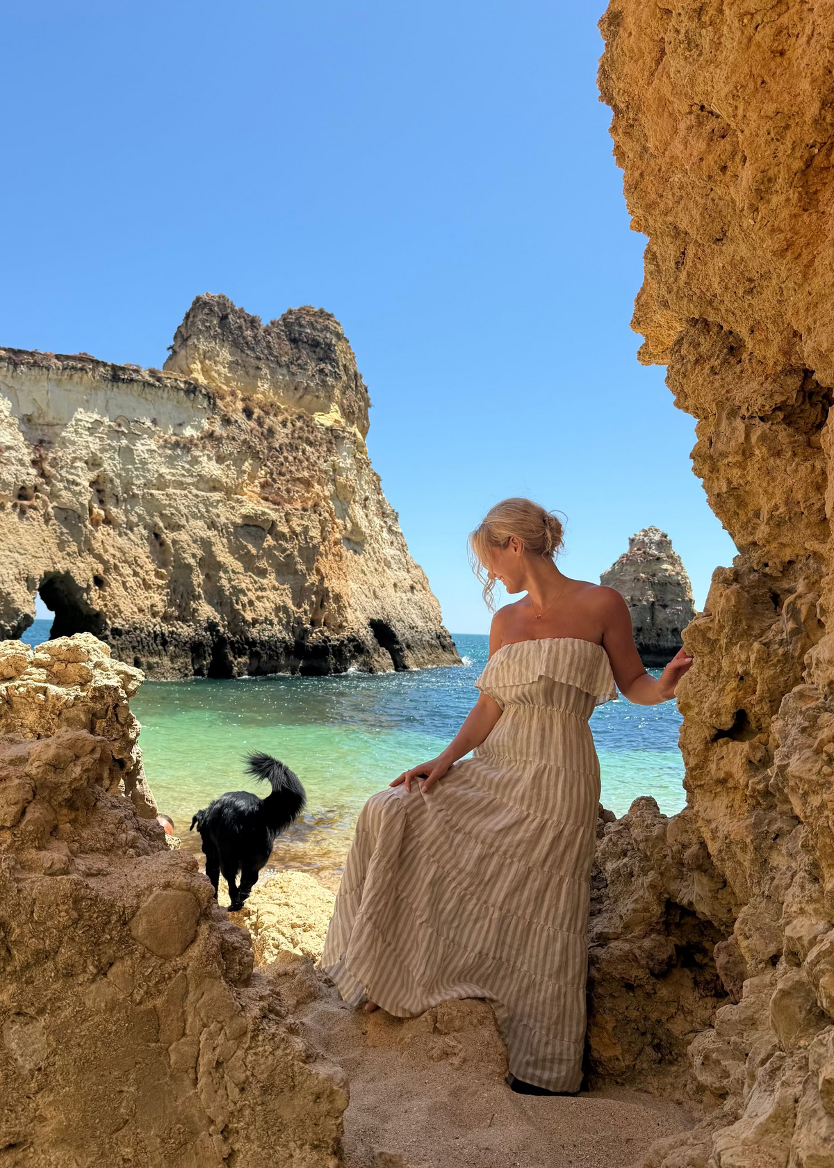 Woman in a Bohomey long linen dress standing on a rocky beach with a castle in the background