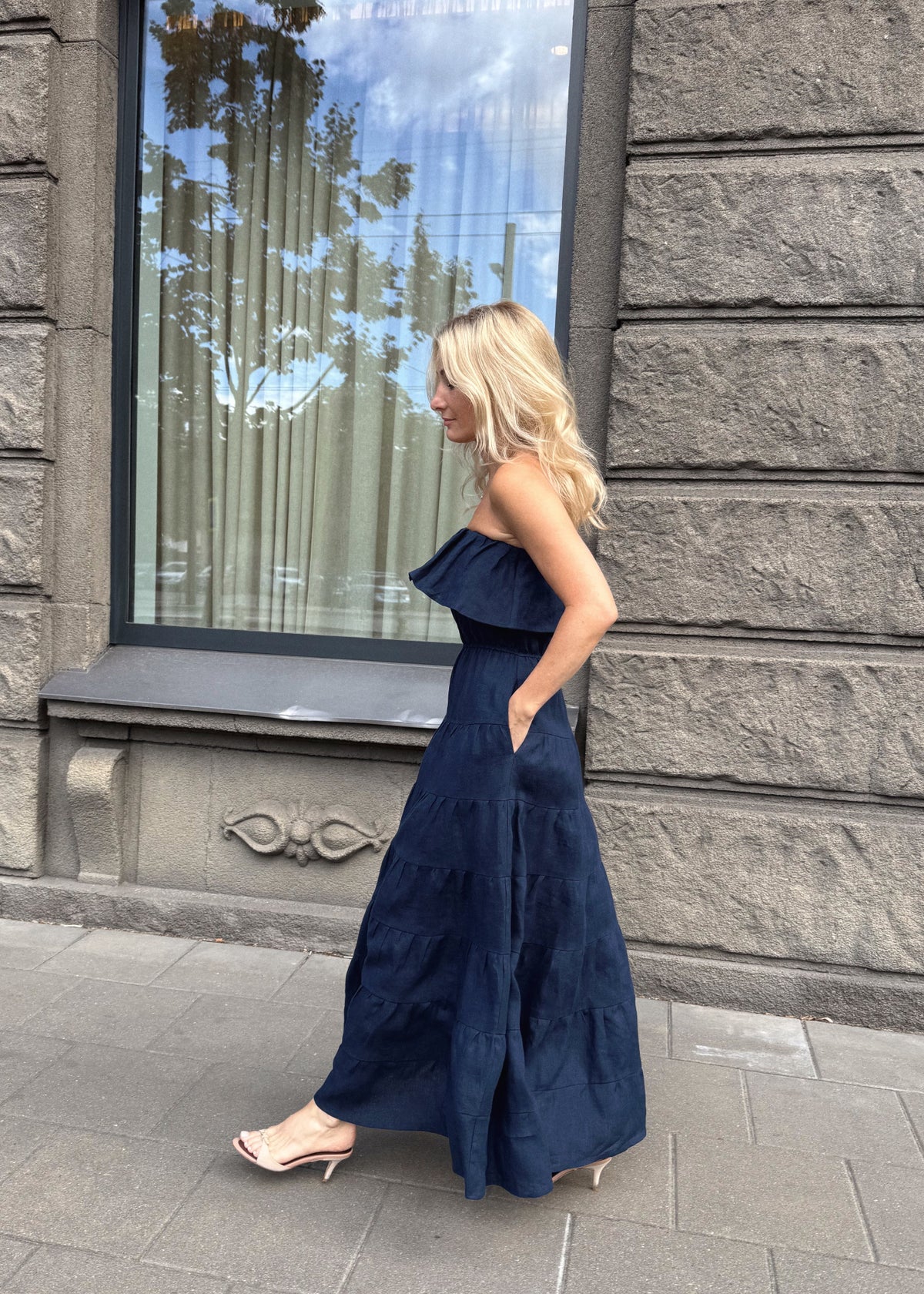 Woman in a Bohomey navy blue linen dress standing on a sidewalk with a stone building in the background