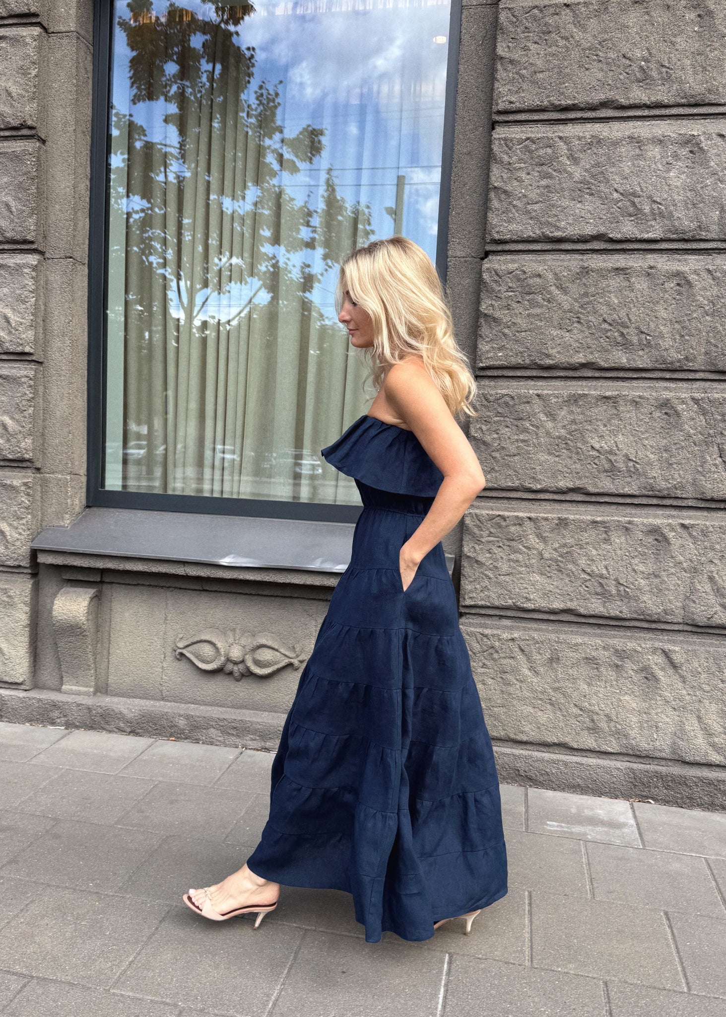 Woman wearing a Bohomey navy blue strapless linen dress on a sidewalk.