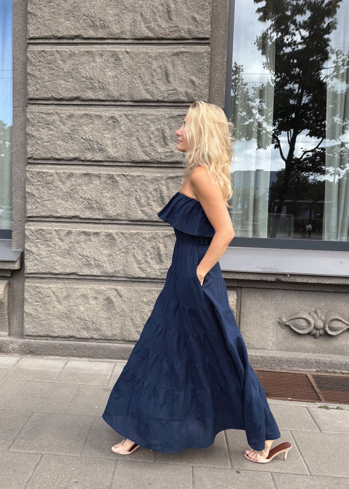 Woman in a Bohomey navy blue maxi linen  dress standing in front of a stone building with large windows.