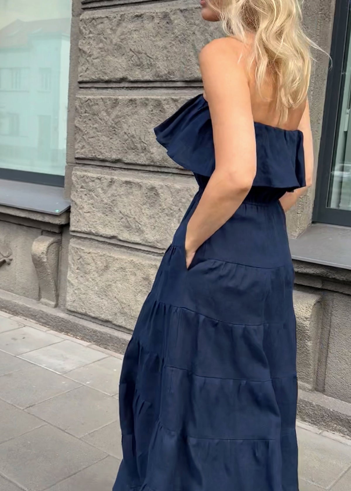 Woman in a Bohomey navy blue maxi linen strapless dress standing on a sidewalk with a building in the background