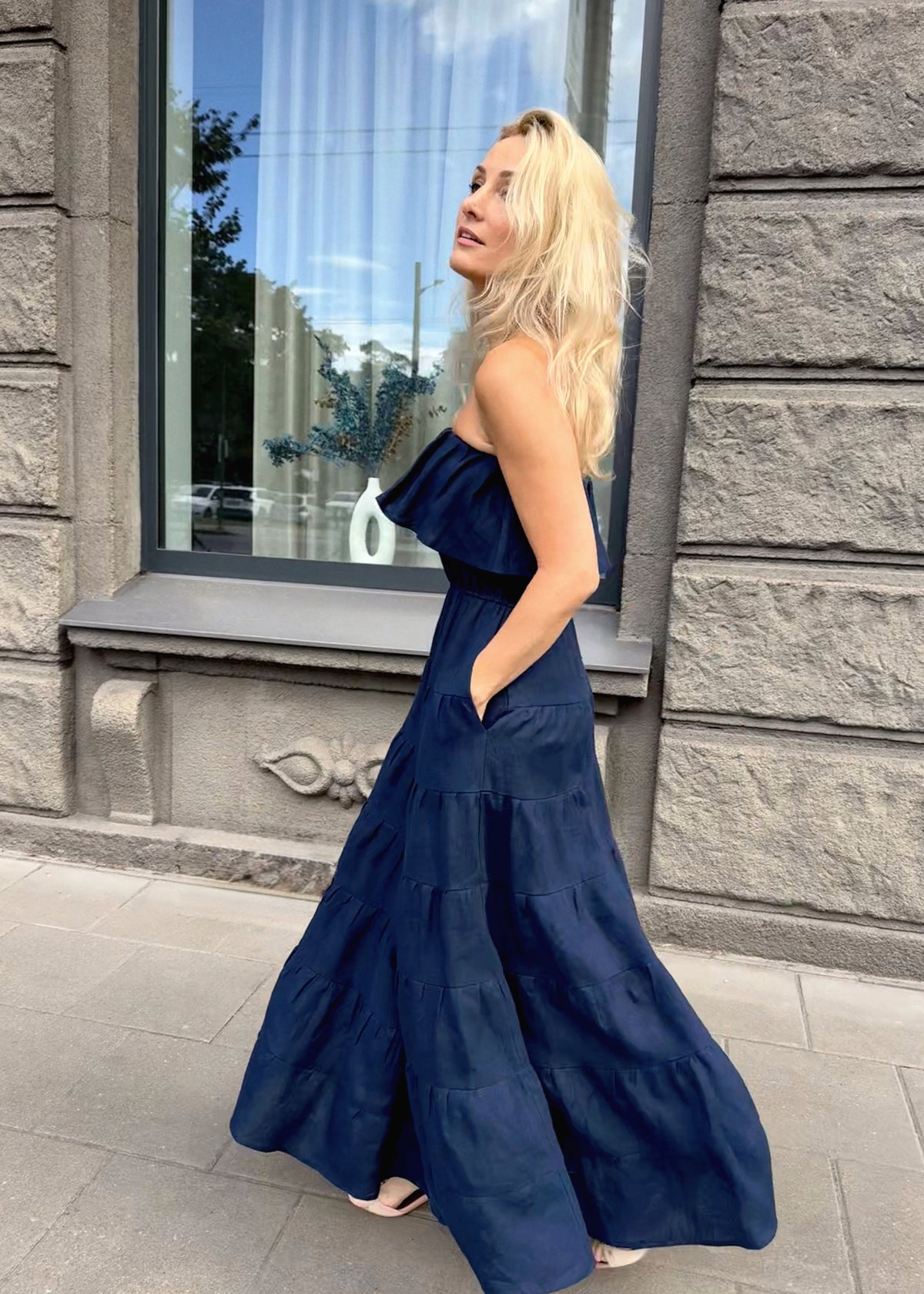 Woman in a Bohomey navy blue maxi linen dress standing outside a building with stone walls.