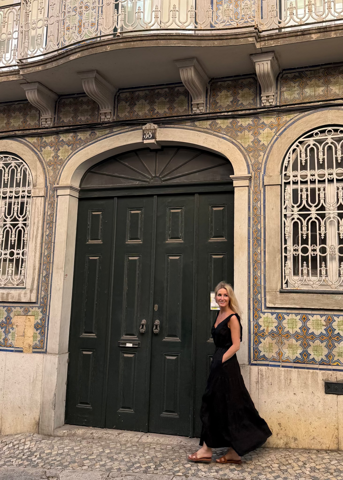 Woman in a Bohomey black linen dress standing in front of a colorful tiled building with a dark green door.
