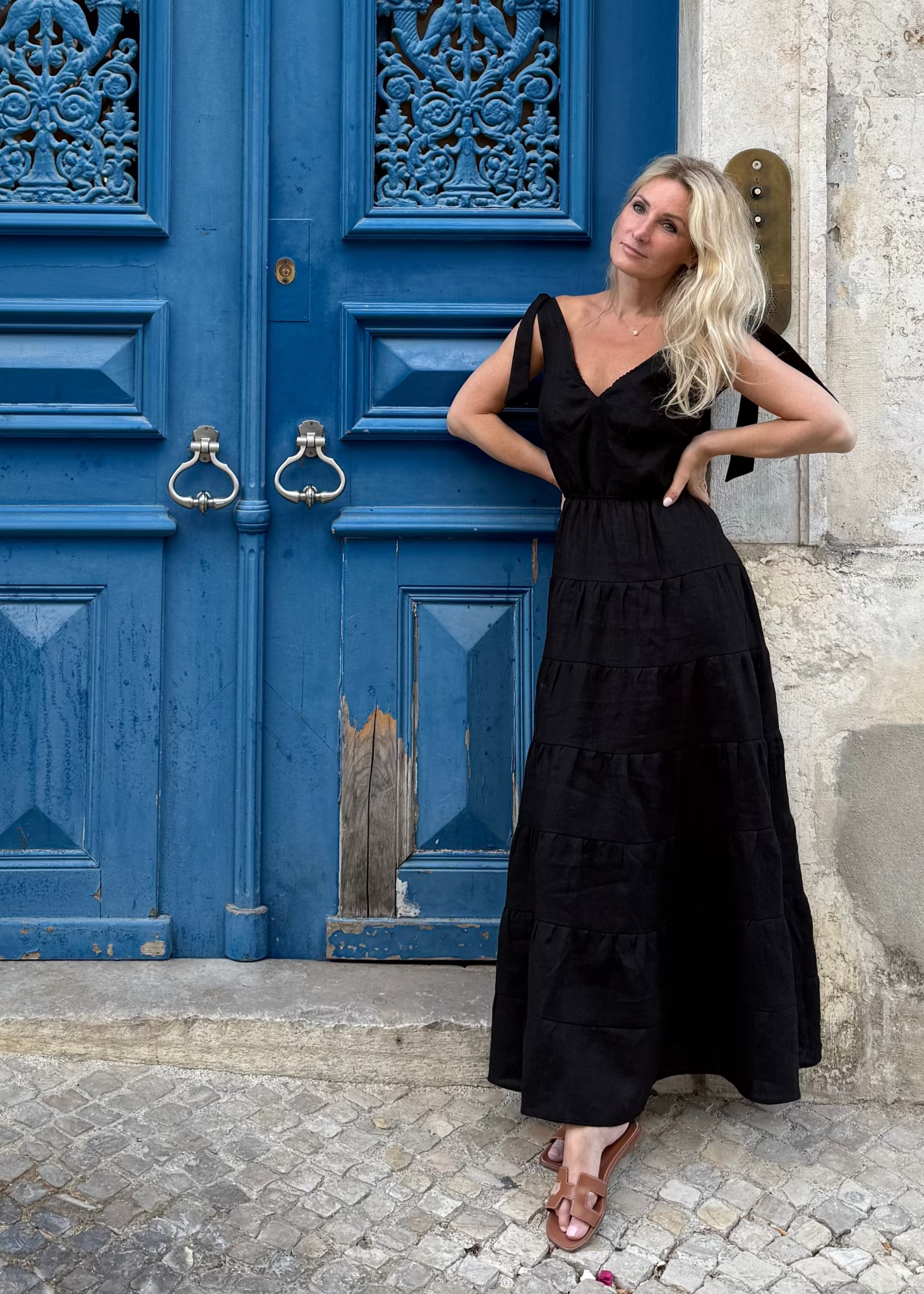Woman in a Bohomey black linen  dress sitting in front of a blue door.