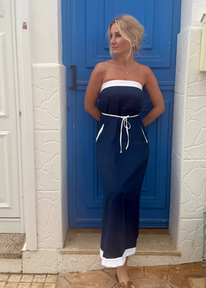 Woman in a navy blue strapless linen dress standing in front of a blue door.