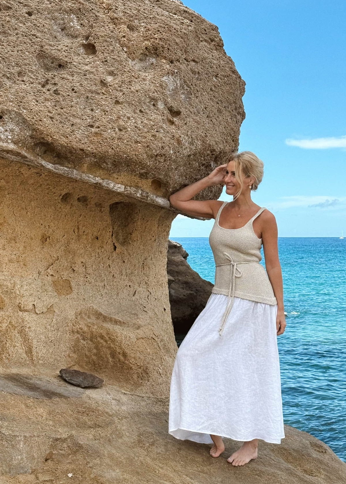 Woman in Bohomey linen dress standing by a large rock with ocean and sky in the background