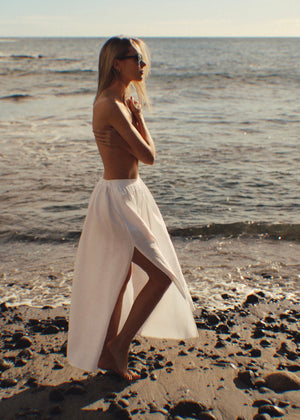 Woman in a white linen skirt standing on a beach with ocean waves in the background