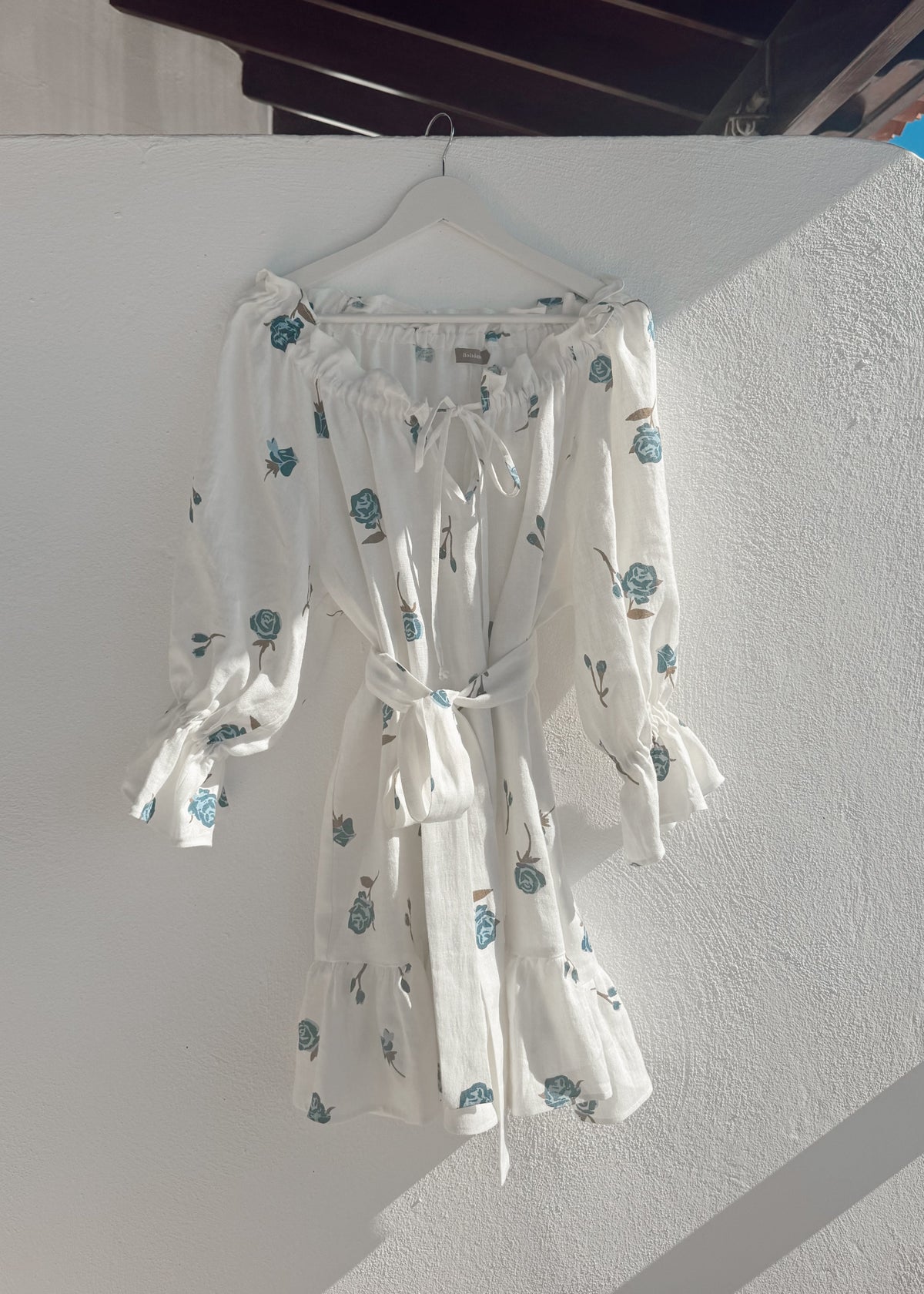 Bohomey white linen dress with blue floral pattern hanging on a white wall