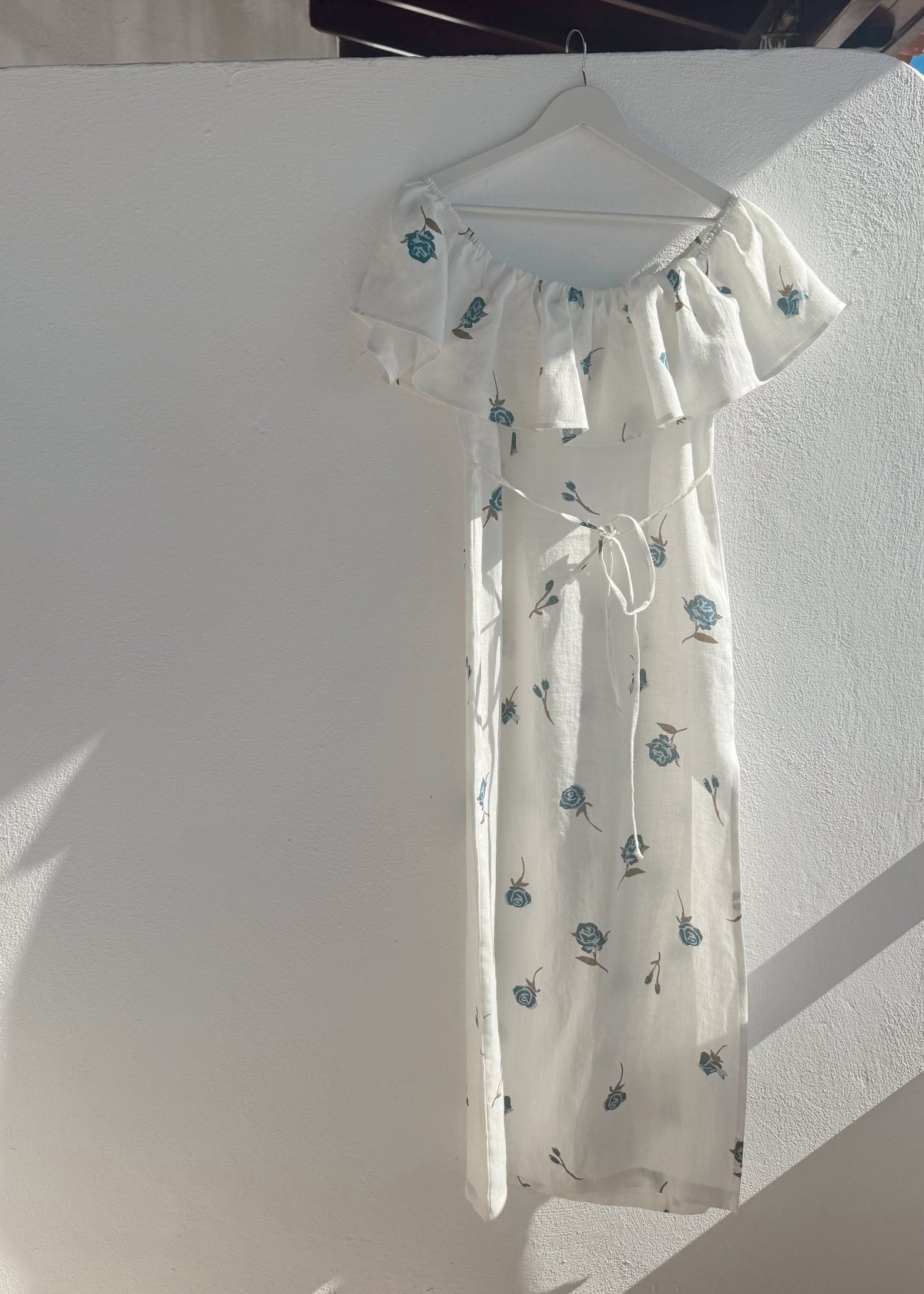 White linen dress with floral pattern on a hanger against a white wall