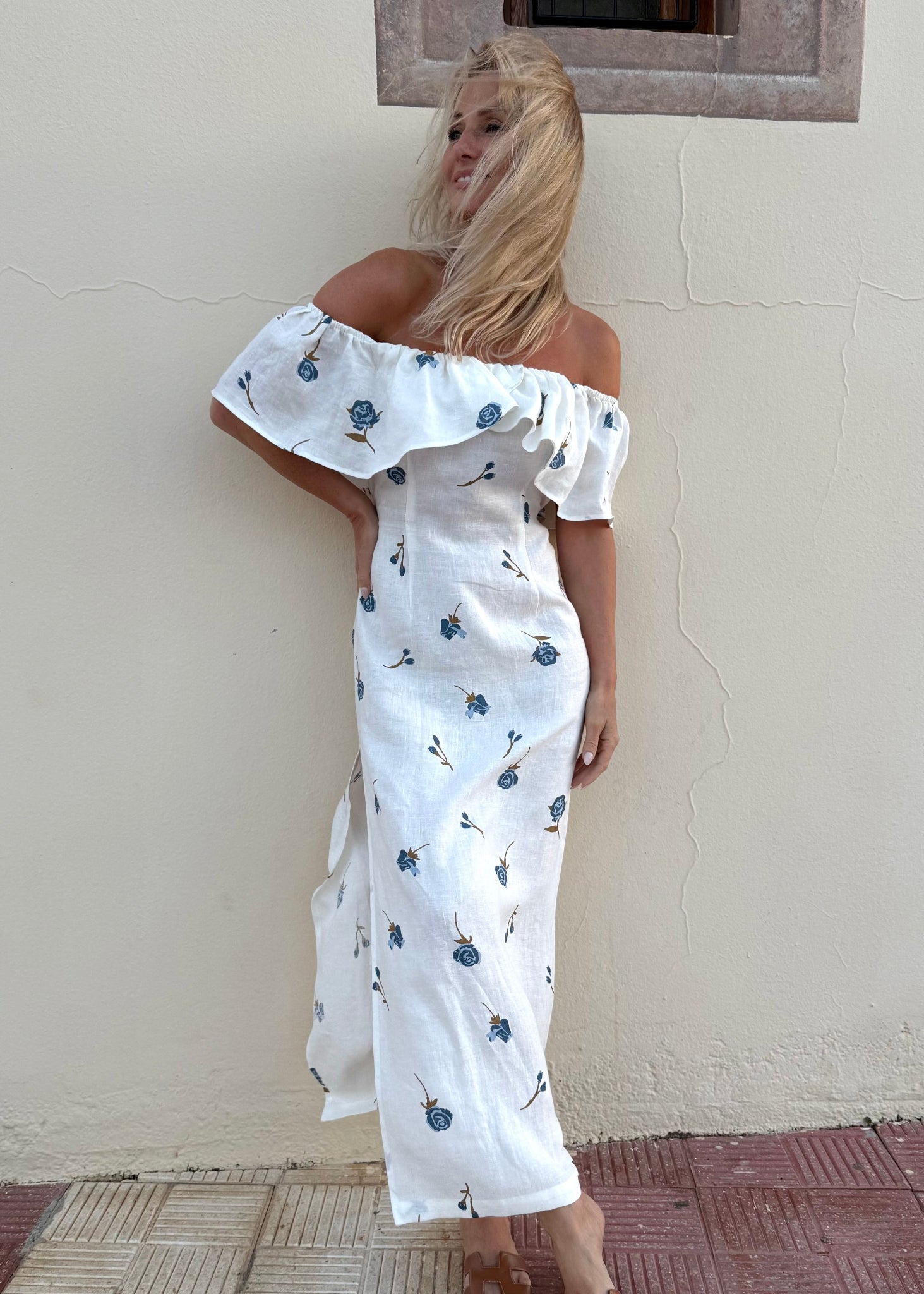 Woman in a white off-shoulder linen dress with blue floral patterns sitting on a boat.