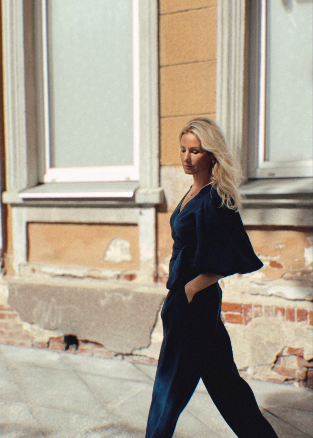 Woman in a navy linen outfit walking on a street with a building in the background
