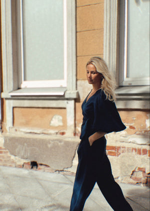Woman in a navy linen outfit walking on a street with a building in the background