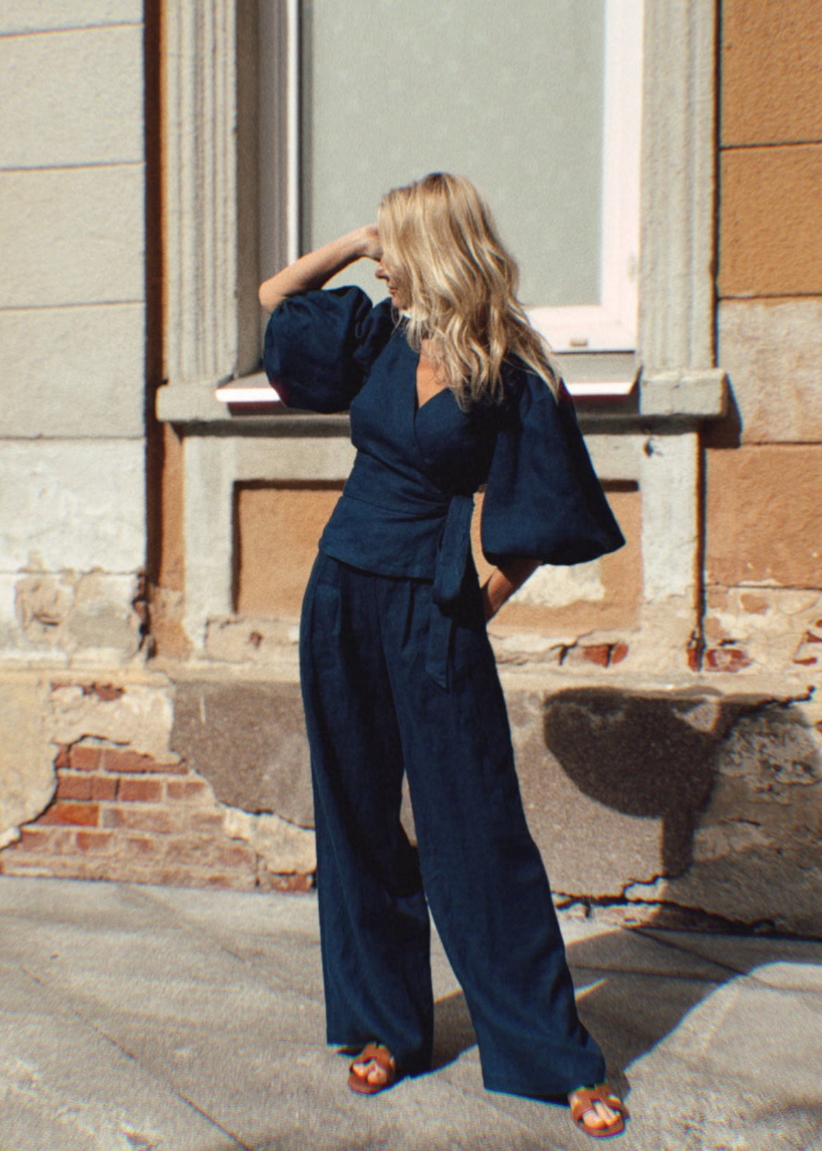 Woman in a navy blue linen outfit standing in front of a textured building.