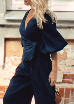 Woman in a navy linen suit standing against a textured wall with large windows.
