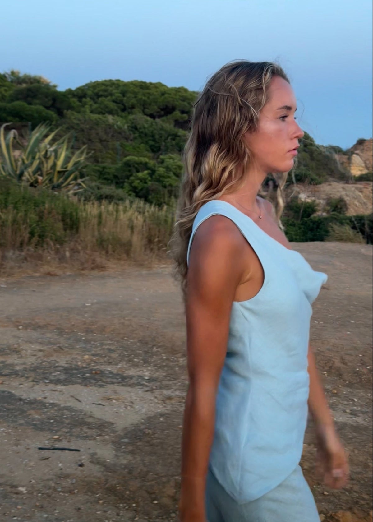 Woman in a light blue dress standing on a path with greenery in the background